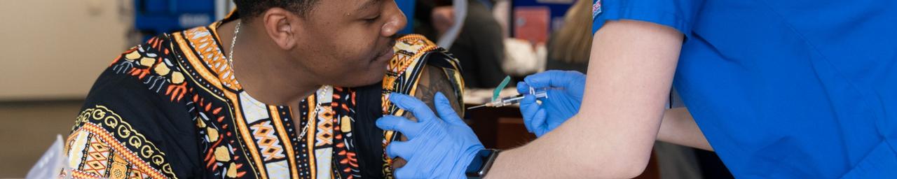 A physician listens to a young man's chest using a stethoscope.